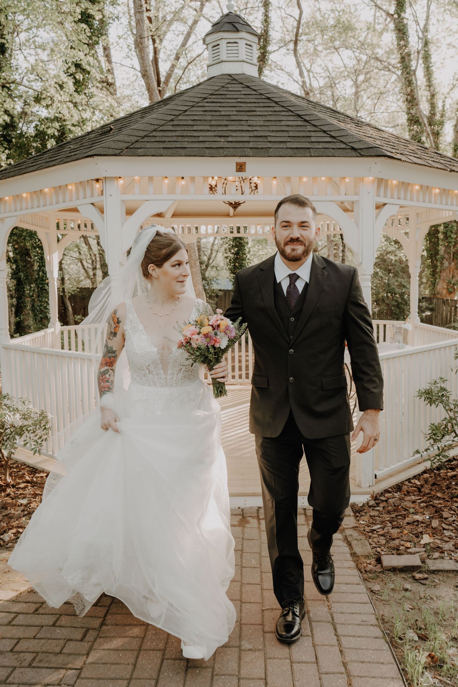 Couple walks together under a white gazebo decorated with string lights.