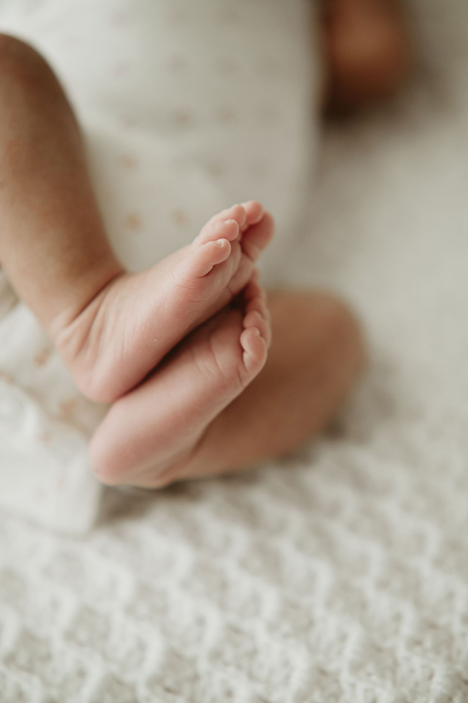 Close-up view of tiny baby feet resting on a textured white blanket in soft natural lighting.
