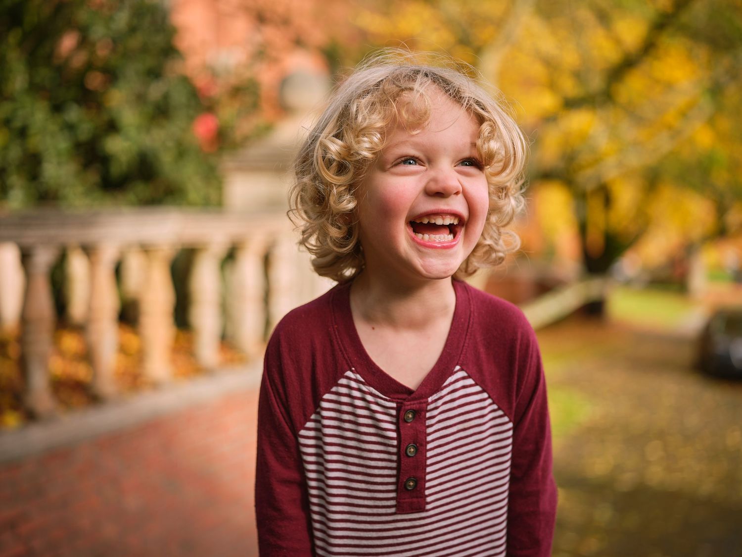 A couple smiles together outdoors in front of an ivy-covered brick building during an autumn engagement photo session.