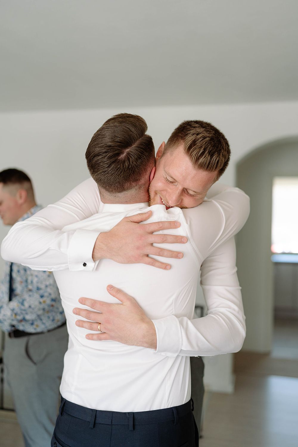Emotional embrace between two people wearing white shirts in a bright indoor space.
