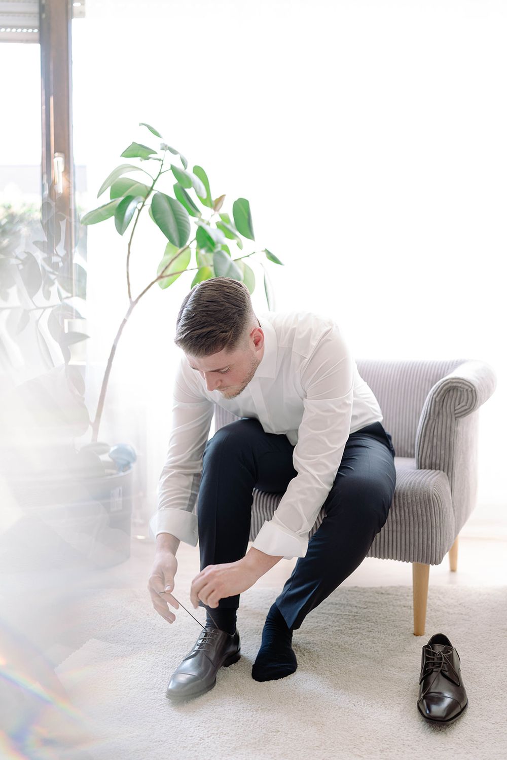 Person in white shirt and dark pants adjusting formal shoes.