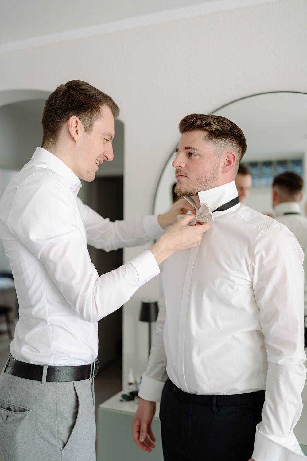 Two people in formal wear helping with clothing adjustments.