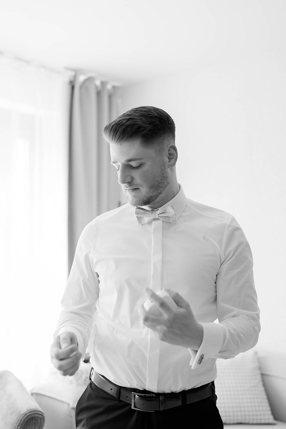 Person in white dress shirt buttoning up formal attire.