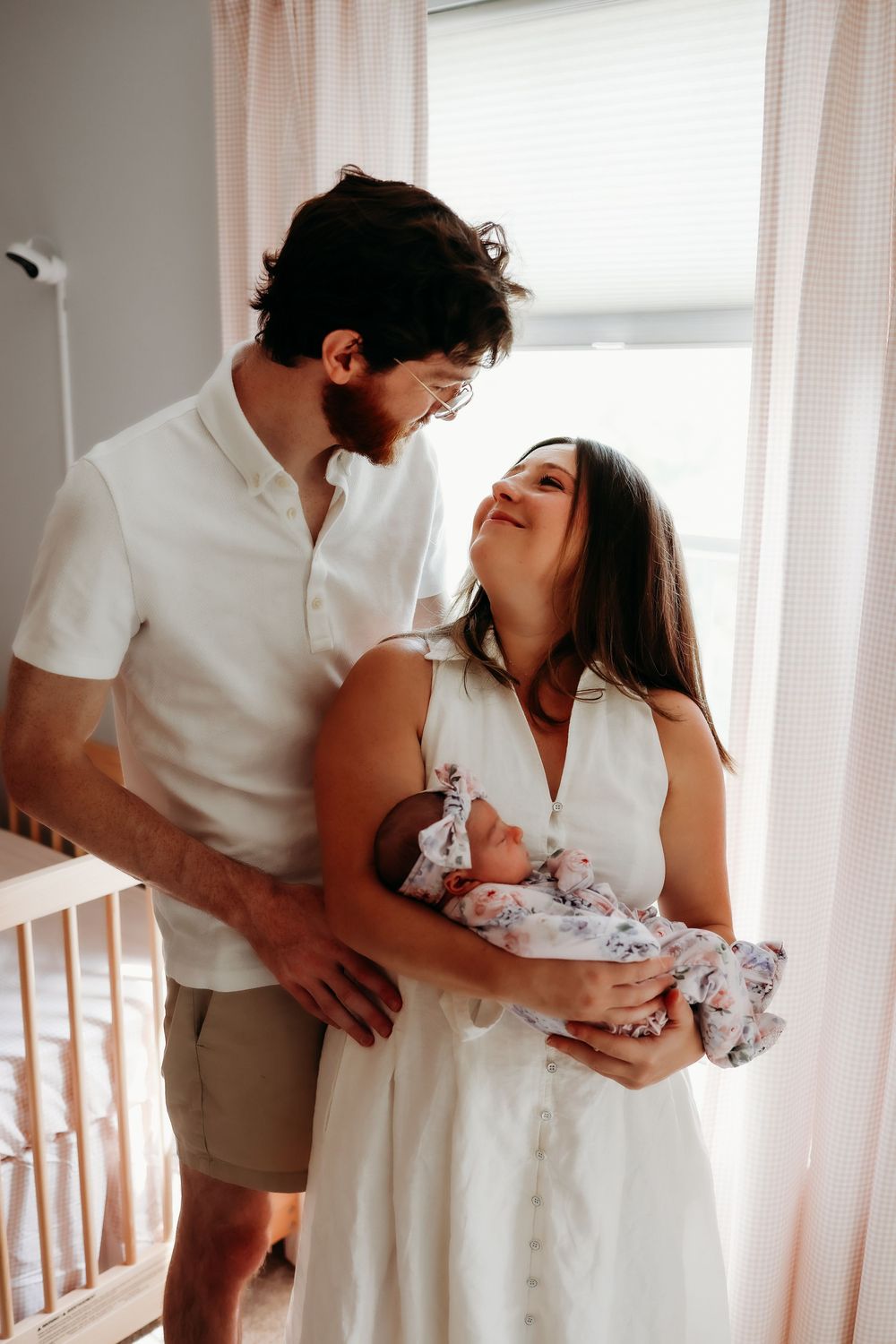 Intimate family portrait showing parents cradling their newborn baby in a sunlit room.