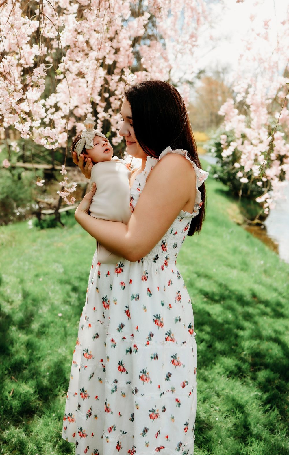 A mother and child in matching floral dresses embrace under blooming cherry blossom trees on a spring day.
