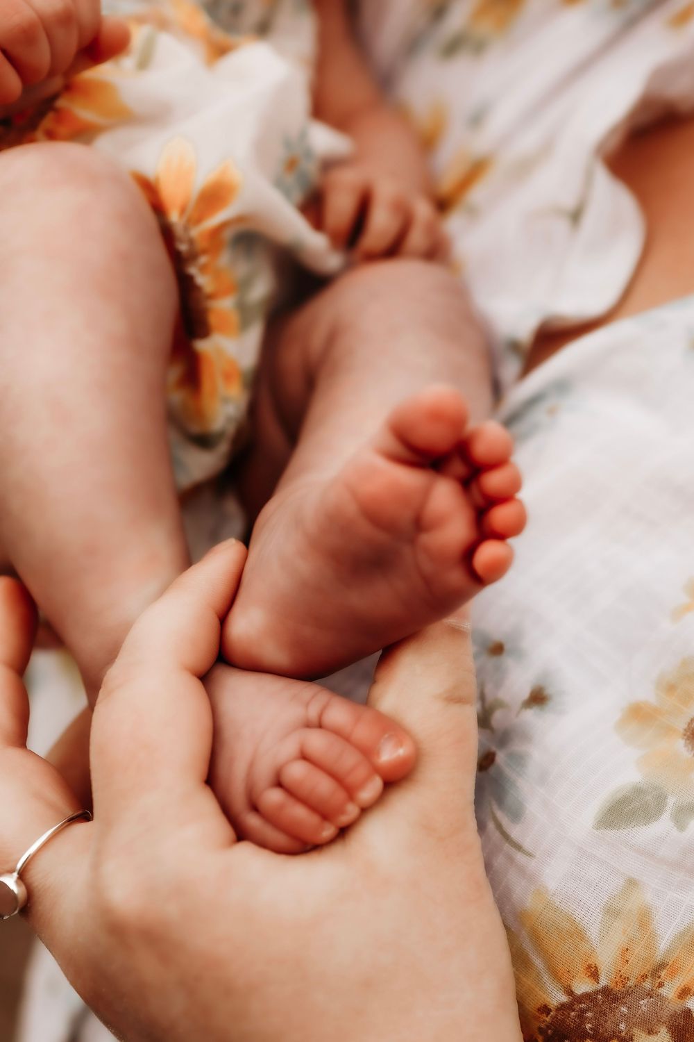 Close up view of a tender moment with tiny baby feet being held by an adult hand on floral patterned fabric.