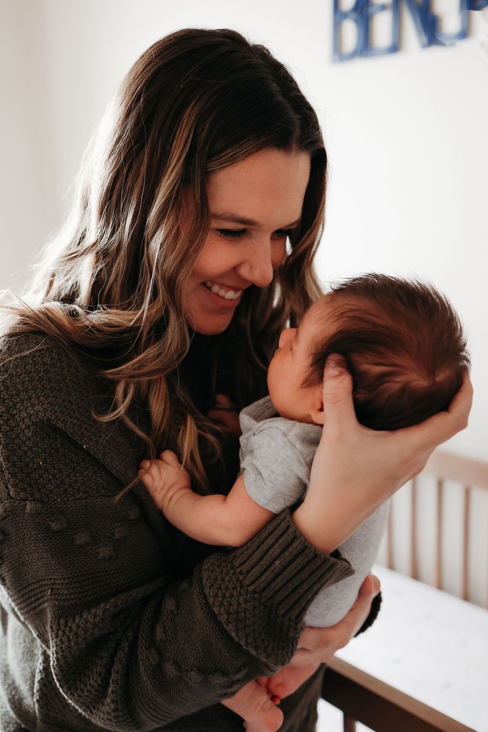 A tender moment shared between mother and newborn as they bond and smile in a nursery room in newborn photoshoot in Roxbury, New Jersey