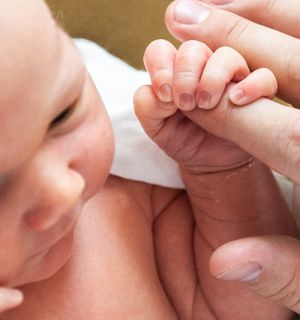 Close-up of tiny newborn hand grasping adult finger in tender moment.
