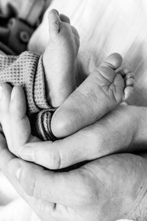 Black and white macro shot of tiny baby foot being gently cradled in adult hand.