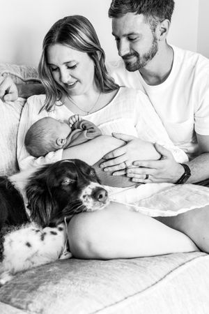Family moment at home with newborn baby and dog on couch.