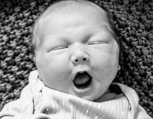 Black and white portrait of yawning newborn on textured knit blanket.