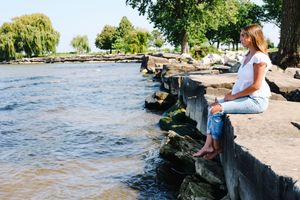 Casual waterfront photoshoot on rocky shore with boats visible in background.