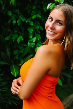 Outdoor portrait series featuring bright orange top against lush green foliage background.