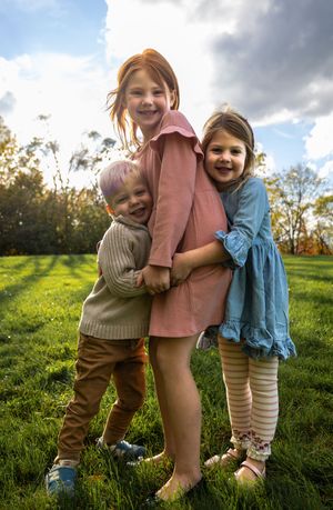 Children hugging and playing together on grass during golden hour with dramatic clouds in background.