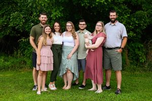 Family group portrait outdoors with everyone dressed in complementary pink and neutral tones.