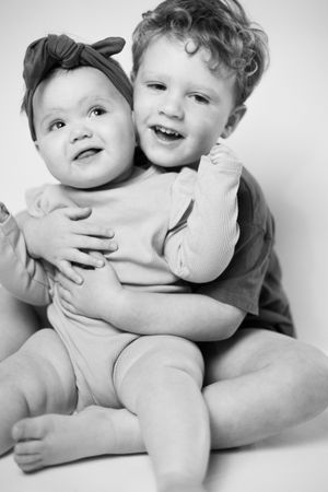 Sweet black and white studio portrait of siblings sharing an affectionate moment together.