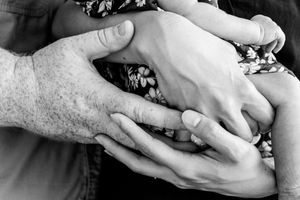 Black and white detail of gentle hands cradling newborn baby.