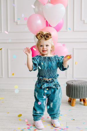 Small child in teal outfit celebrating with pink and white balloons and confetti.