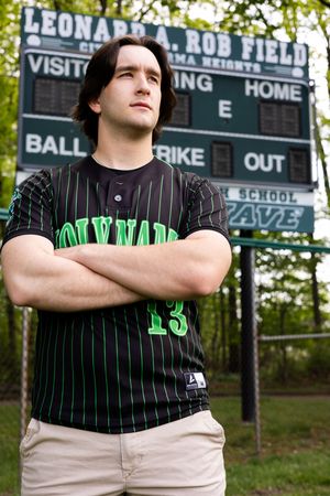 Baseball player in pinstriped uniform poses confidently on field with scoreboard in background.