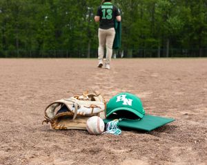 Baseball equipment including glove, ball and cap scattered on dirt infield.