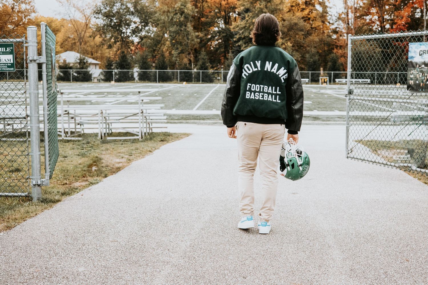 A person walking on a path wearing a dark athletic jacket and holding sports equipment.