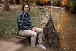 A relaxed outdoor photo session on a stone wall with autumn trees and water in the background.
