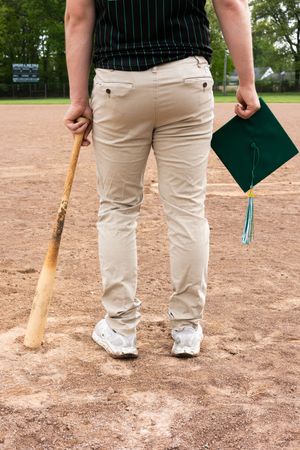 Baseball player in pinstripes and khakis stands with bat on dirt field.