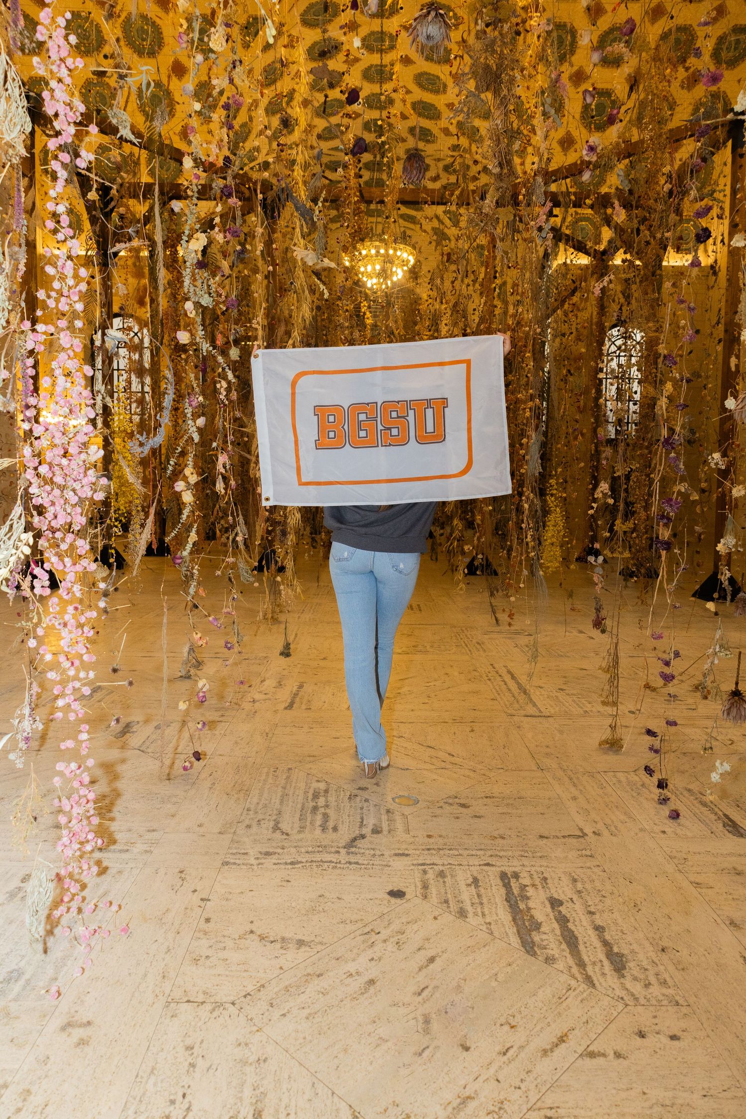 A creative photo with someone holding a sign in a golden-lit room with hanging decorations.
