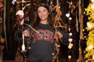 A casual portrait in a decorated room wearing a college sweatshirt with hanging lights.