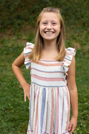 Portrait series in striped summer dress with ruffled sleeves against green natural background.