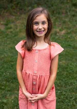 Portrait sequence in coral pink smocked dress with cap sleeves against natural green backdrop.