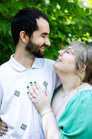 Happy couple shares intimate moments outdoors against a backdrop of green leaves.