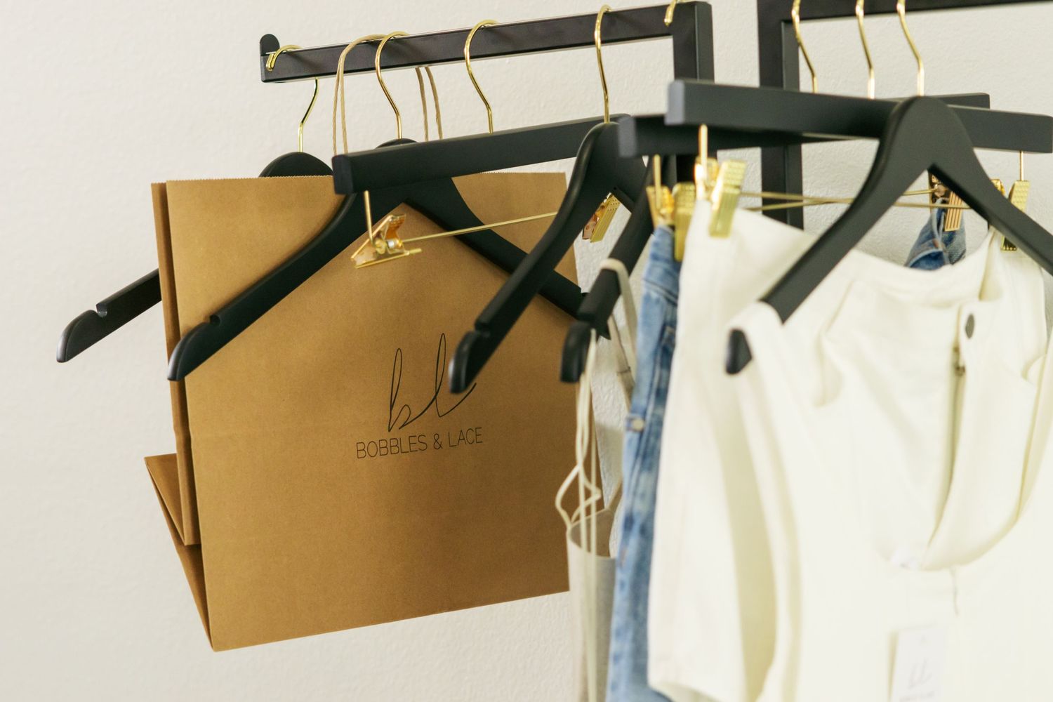 A close up of a rack of hangers, some are empty, some with merchandise, and one  branded tote bag hanging in between.