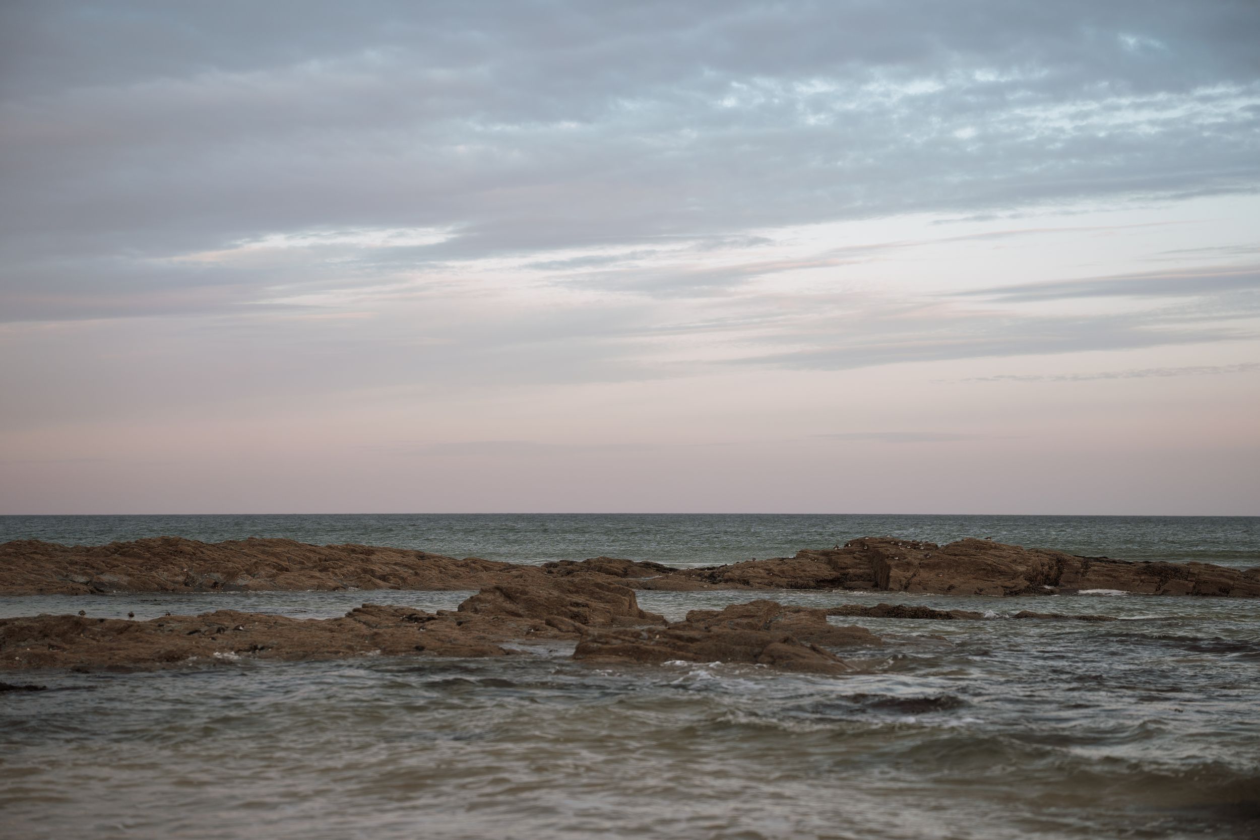 Rocky coastline with choppy waves meets a moody sky during sunset creating a serene seascape view.