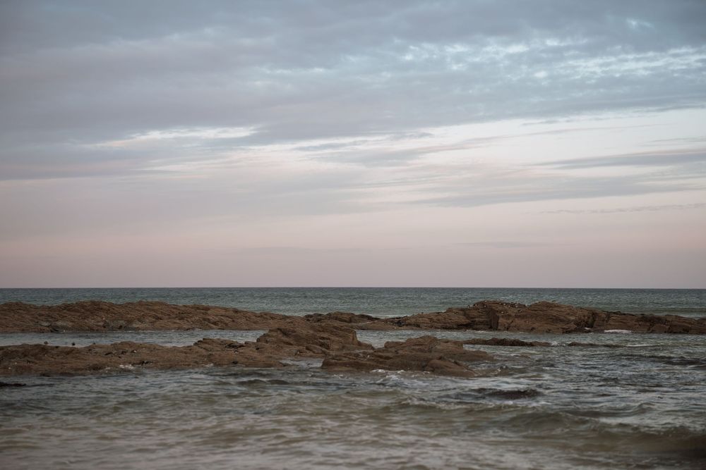 Rocky coastline with choppy waves meets a moody sky during sunset creating a serene seascape view.