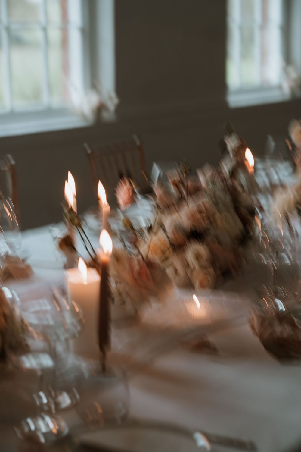 Soft focus candlelit table setting with white linens and decorative floral arrangements creating an intimate dining atmosphere.