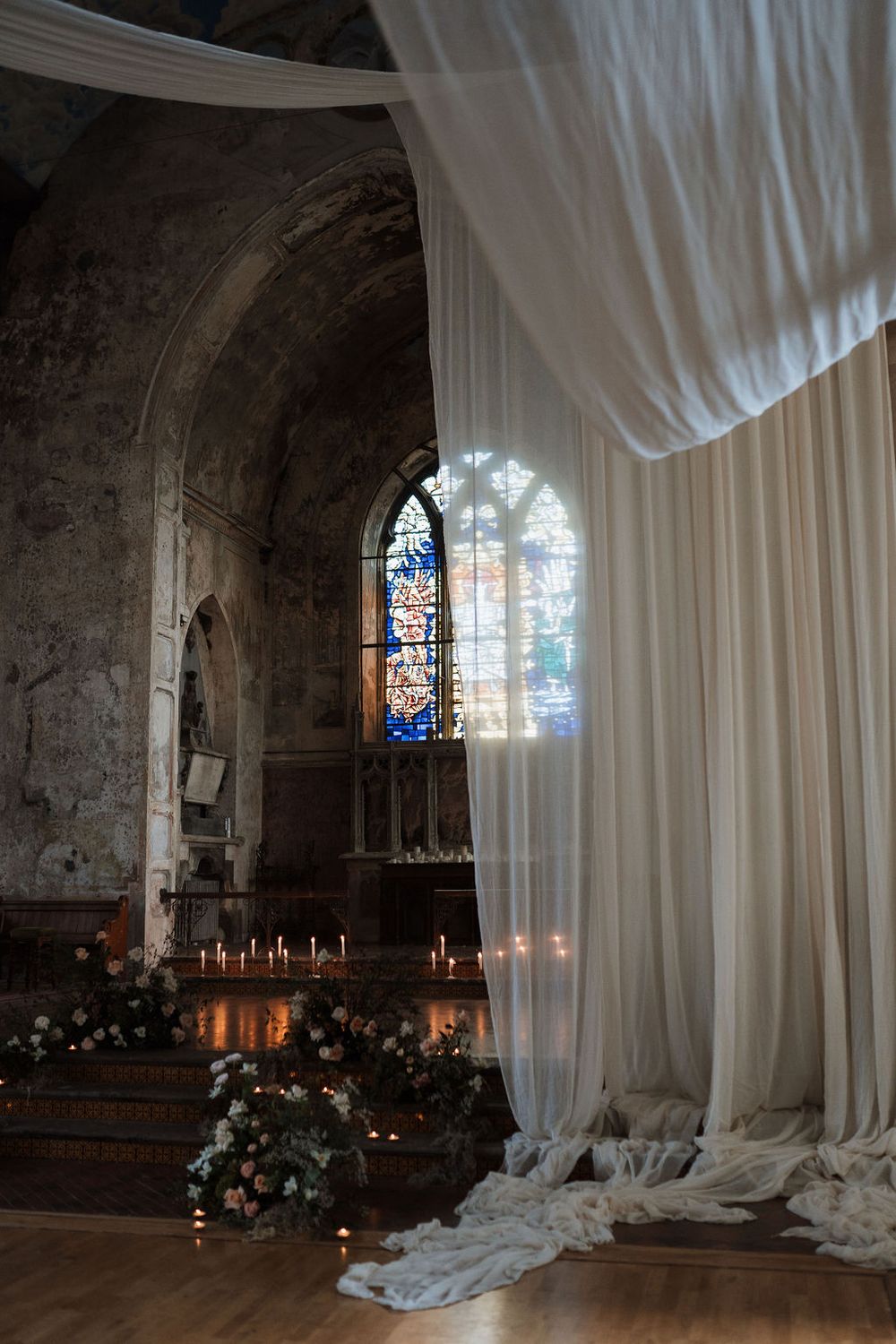 Elegant church interior with flowing white drapes, stained glass window, and glowing candles creating a romantic atmosphere.