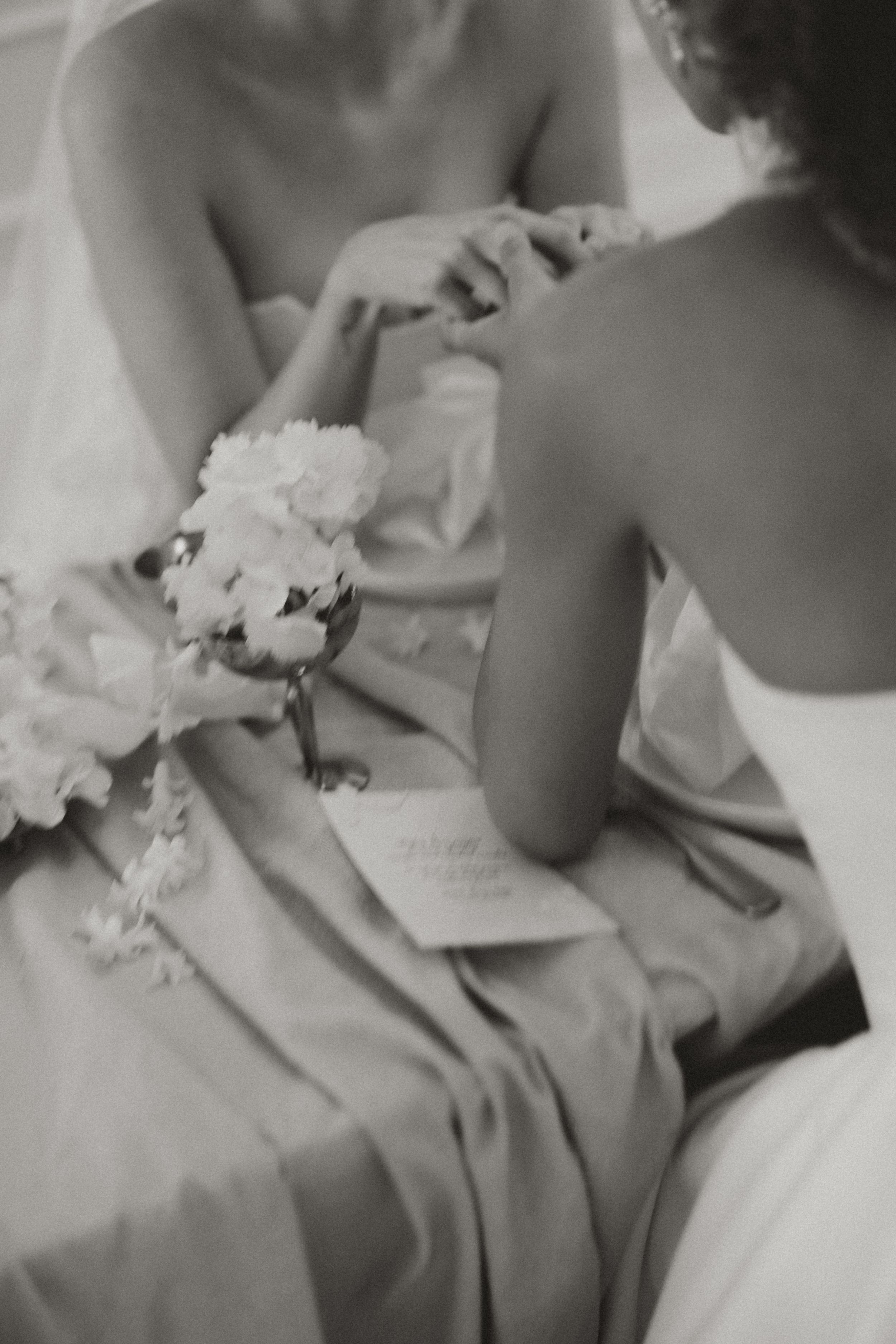 Black and white moment captured at a wedding showing flowers and dress details as someone writes a note or letter.