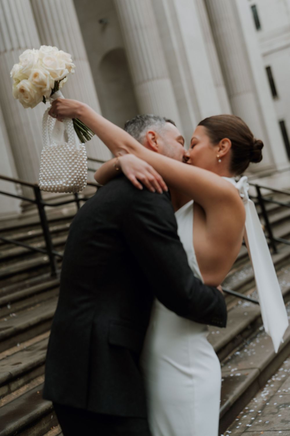 Newlyweds share an intimate moment on stone steps as bride holds a white bouquet against a classical architectural backdrop of marylebone