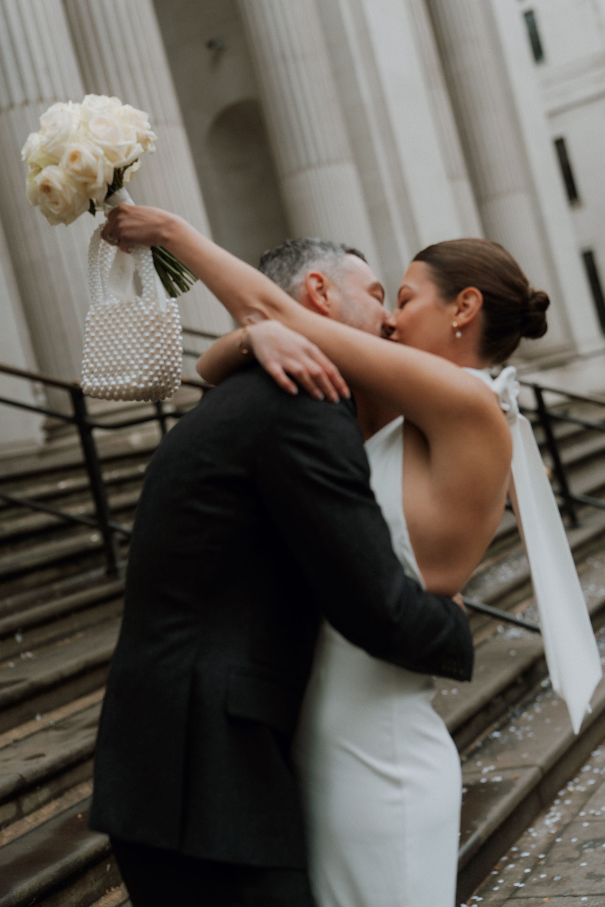 Newlyweds share an intimate moment on stone steps as bride holds a white bouquet against a classical architectural backdrop of marylebone