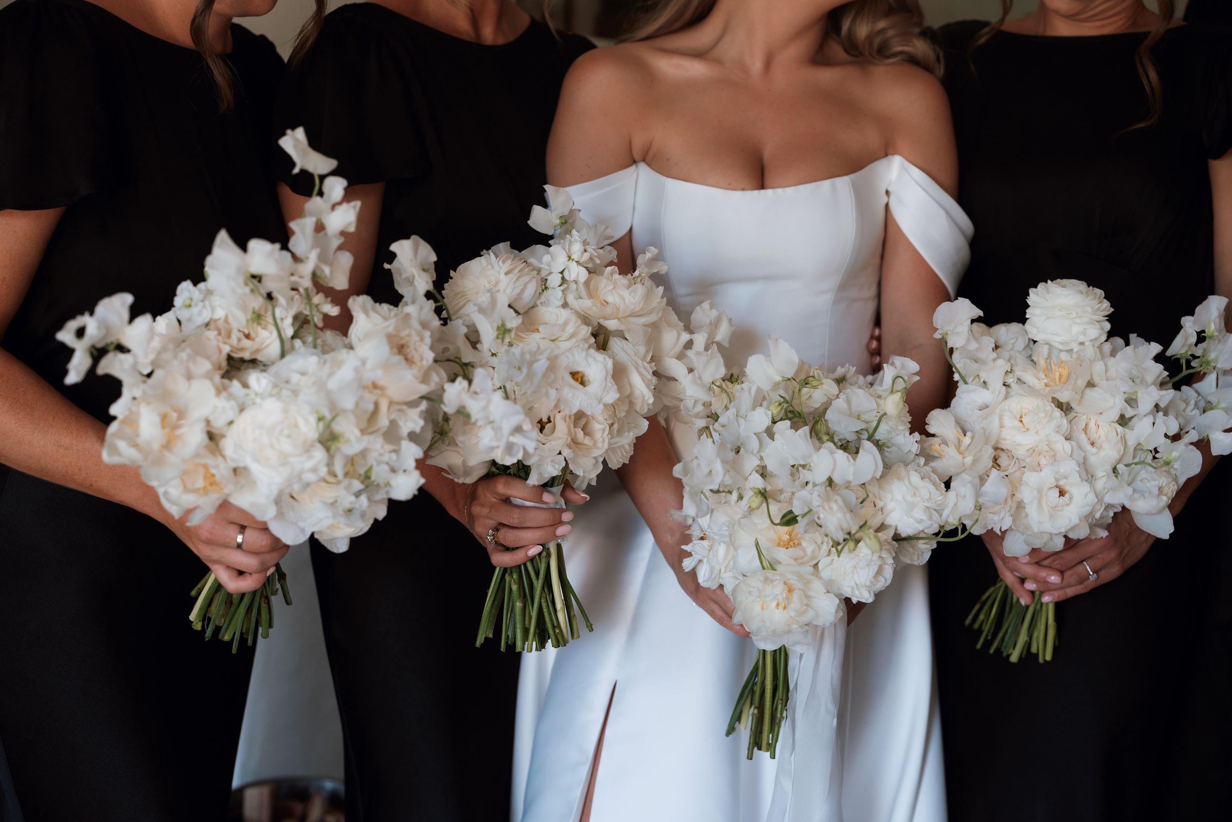 Three elegant white floral bouquets held against black and white dresses at a formal wedding celebration.