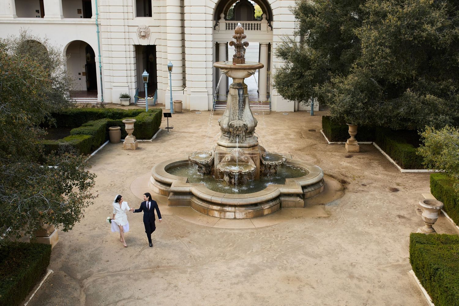 An elegant stone fountain stands in a courtyard surrounded by classic architecture and manicured landscaping.