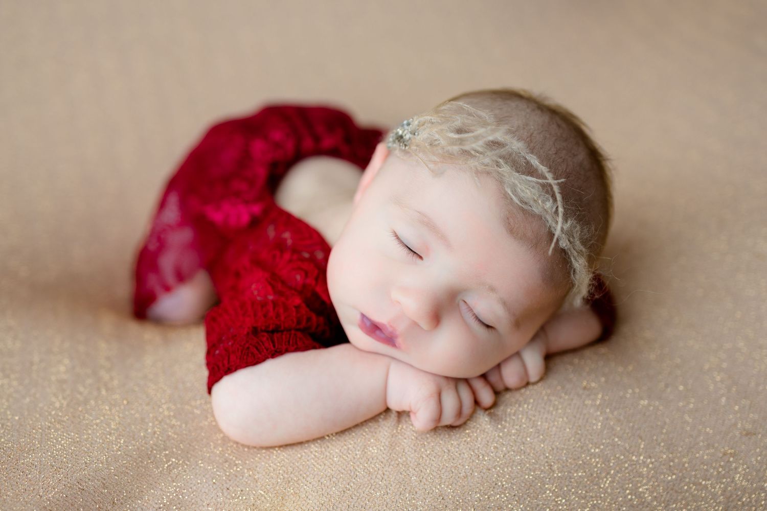 Sleeping newborn in red outfit rests peacefully on pale yellow background.