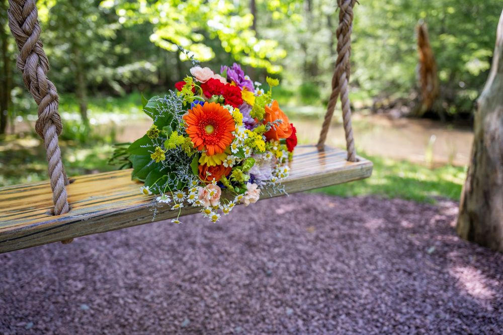 Colorful bouquet of orange gerbera daisies and mixed flowers resting on a wooden rope swing in a lush garden.