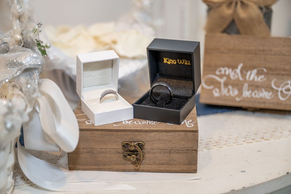 Two wedding rings displayed in open jewelry boxes on a rustic wooden keepsake box at a wedding reception.