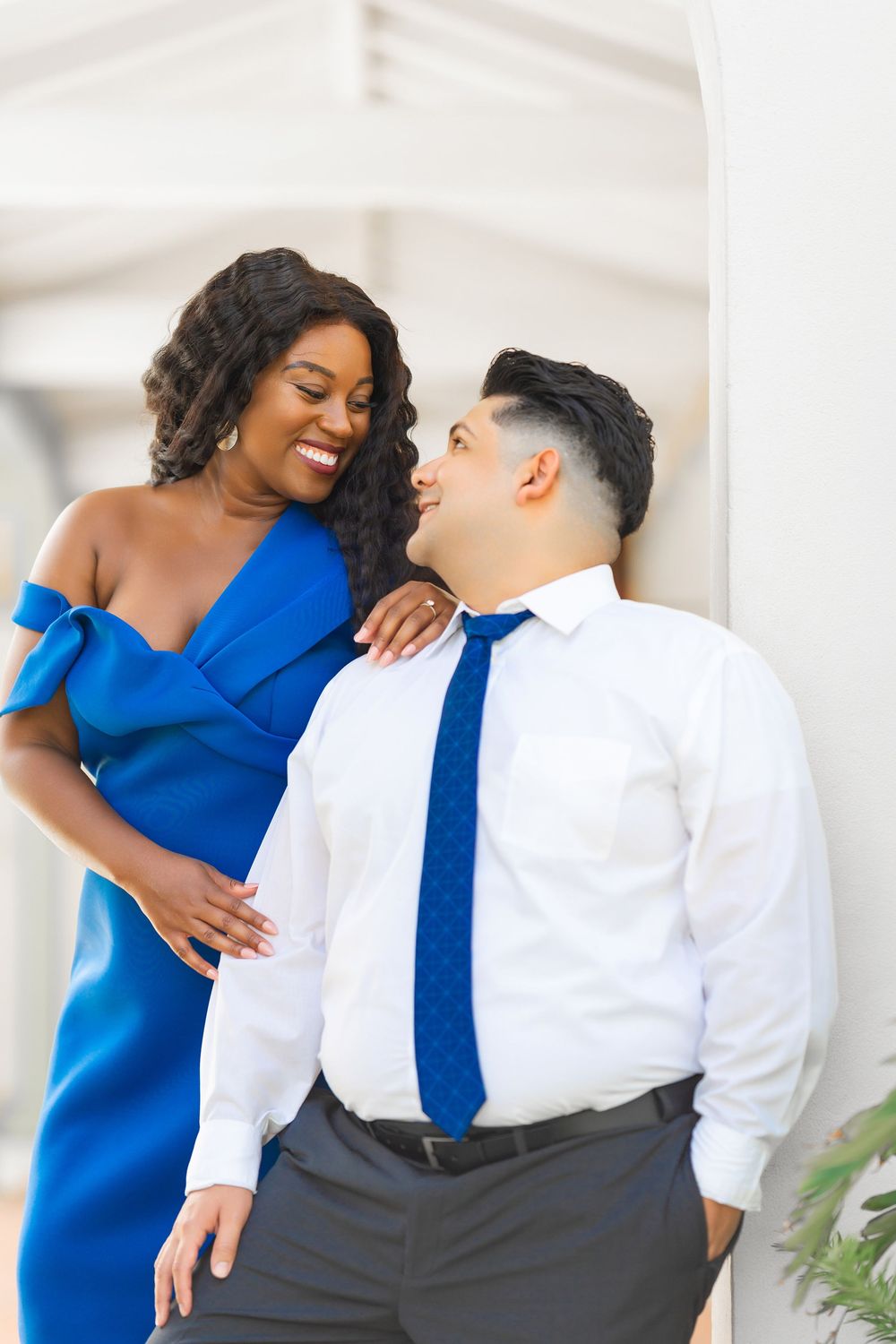 A couple shares a romantic moment, with one wearing a royal blue dress and the other in a white shirt with navy tie.