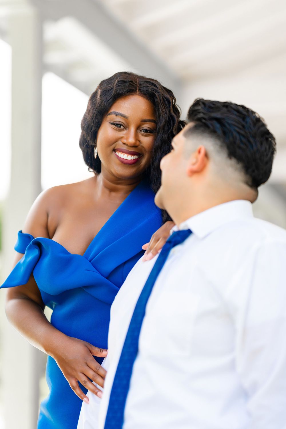 A couple in formal attire share a romantic moment, with one wearing a striking royal blue dress and the other in white shirt.