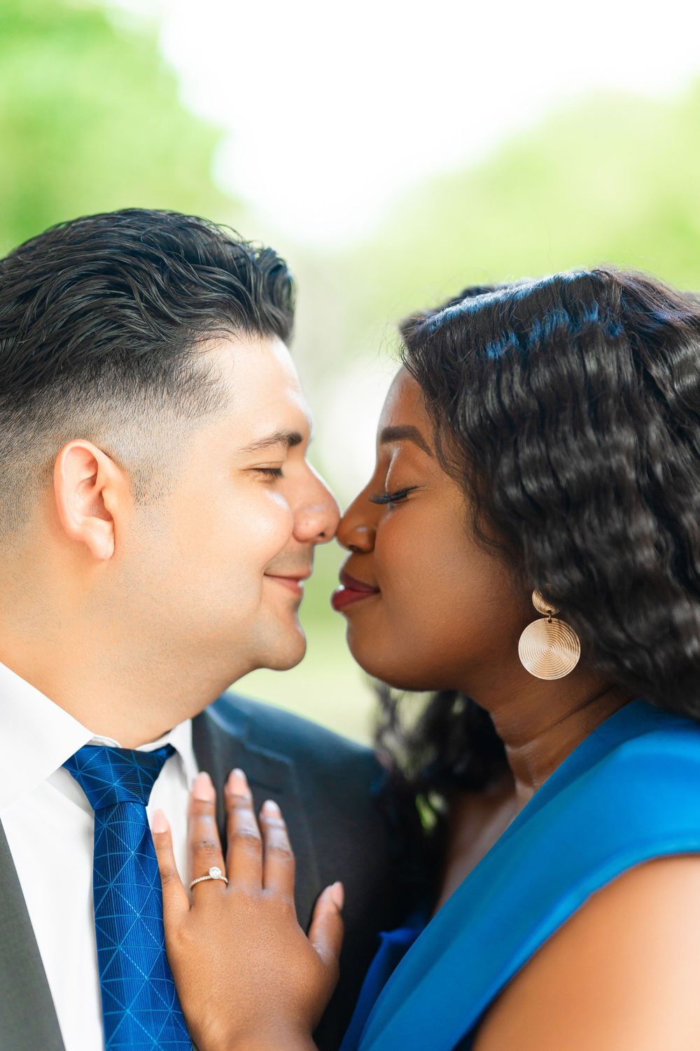 Romantic close-up of couple sharing an intimate moment in bright natural lighting against blurred green background.