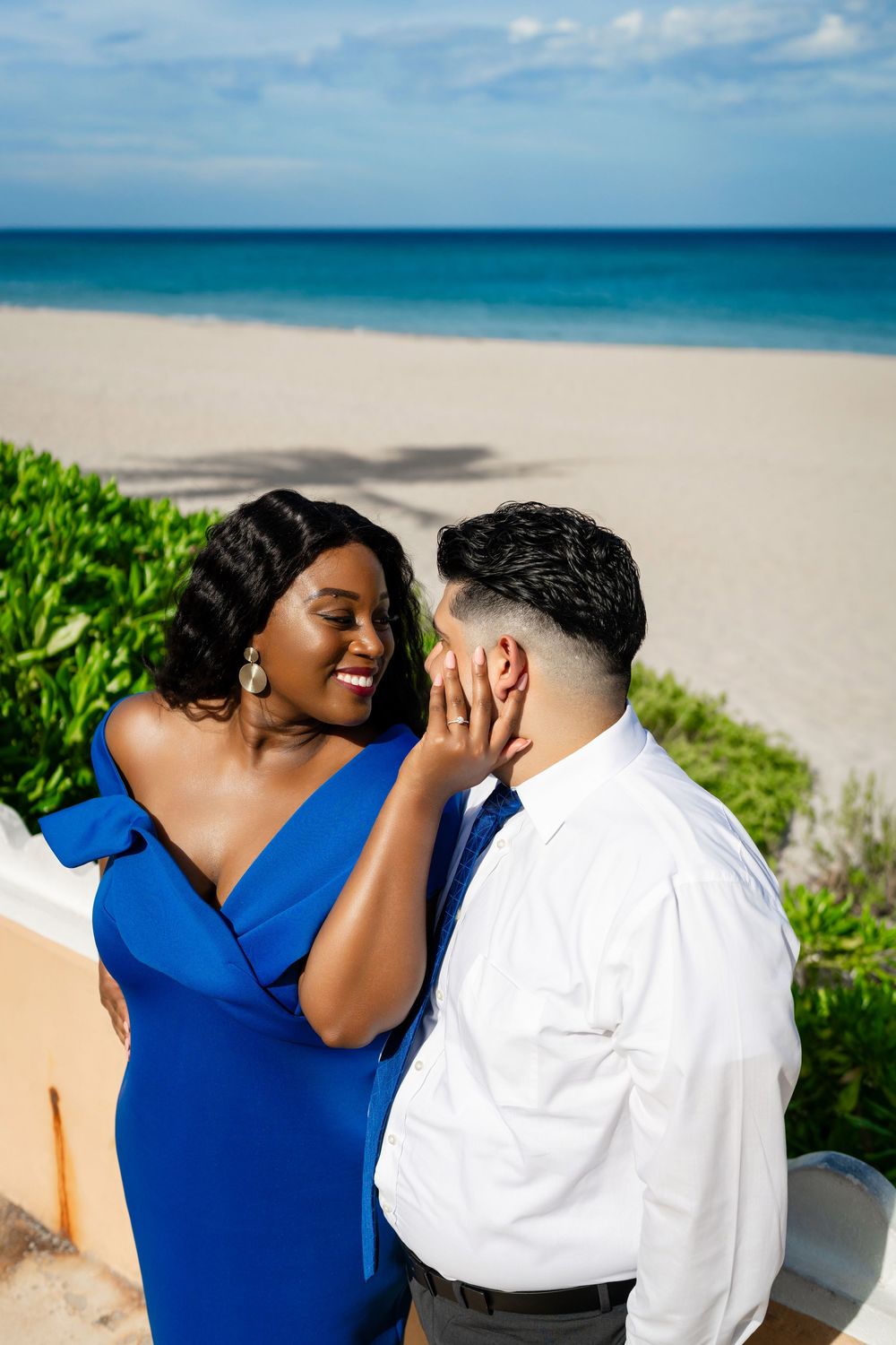 A romantic couple embraces on a scenic beach with crystal blue waters and lush greenery.
