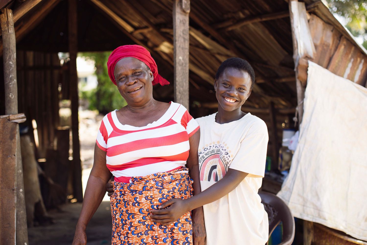 Two people stand together smiling outside a rustic wooden structure in Africa.